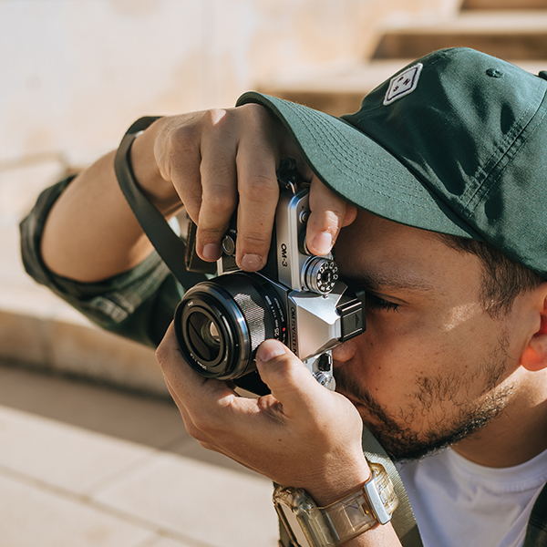 This is a photo of a photographer holding the OM SYSTEM OM-3 camera with the M.ZUIKO DIGITAL 25mm F1.8 II lens attached to the camera body.