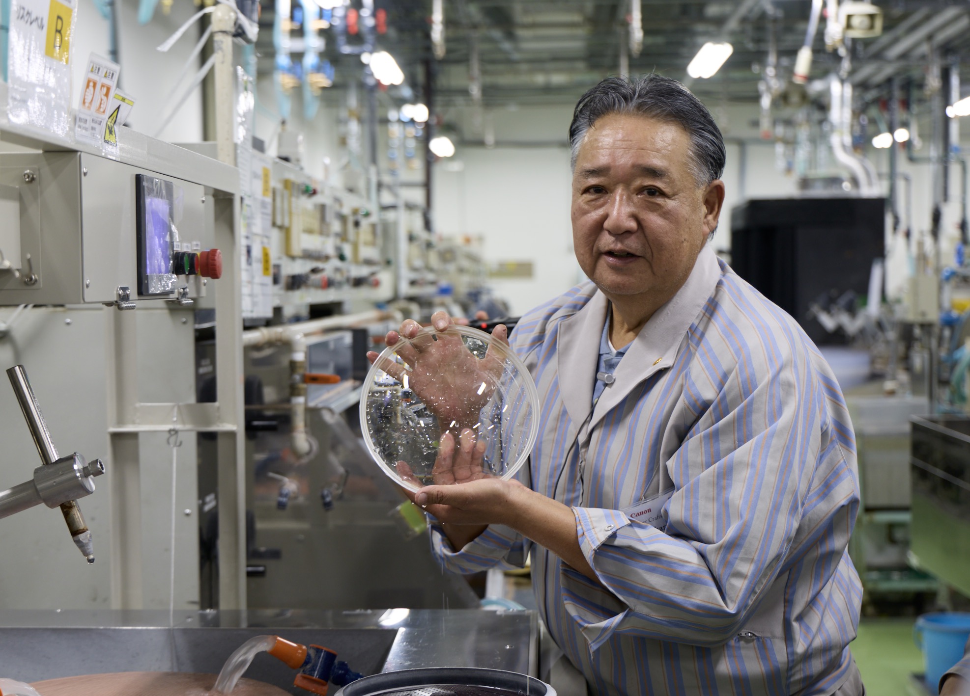 A master lens poilsher in the Caonn lens factory holds up a large glass element. 