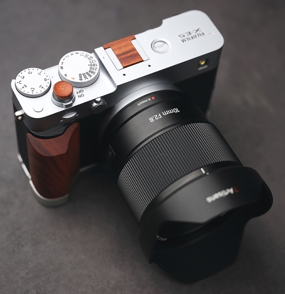 A 7Artisans 10mm F2.8 lens is attached to a Fujifilm X-E5 body, which rests on a gray carpet.