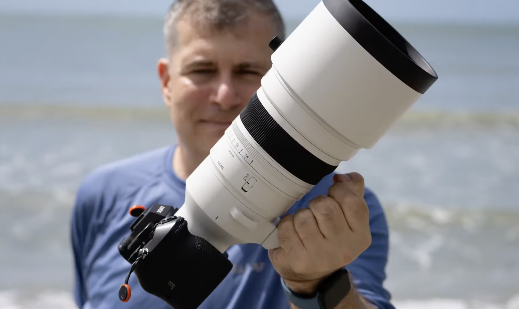 The Sigma 200mm lens being held up to the camera with water behind