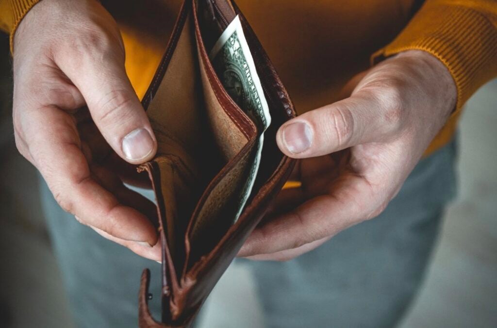 A person holding open a wallet revealing only one dollar bill in it.