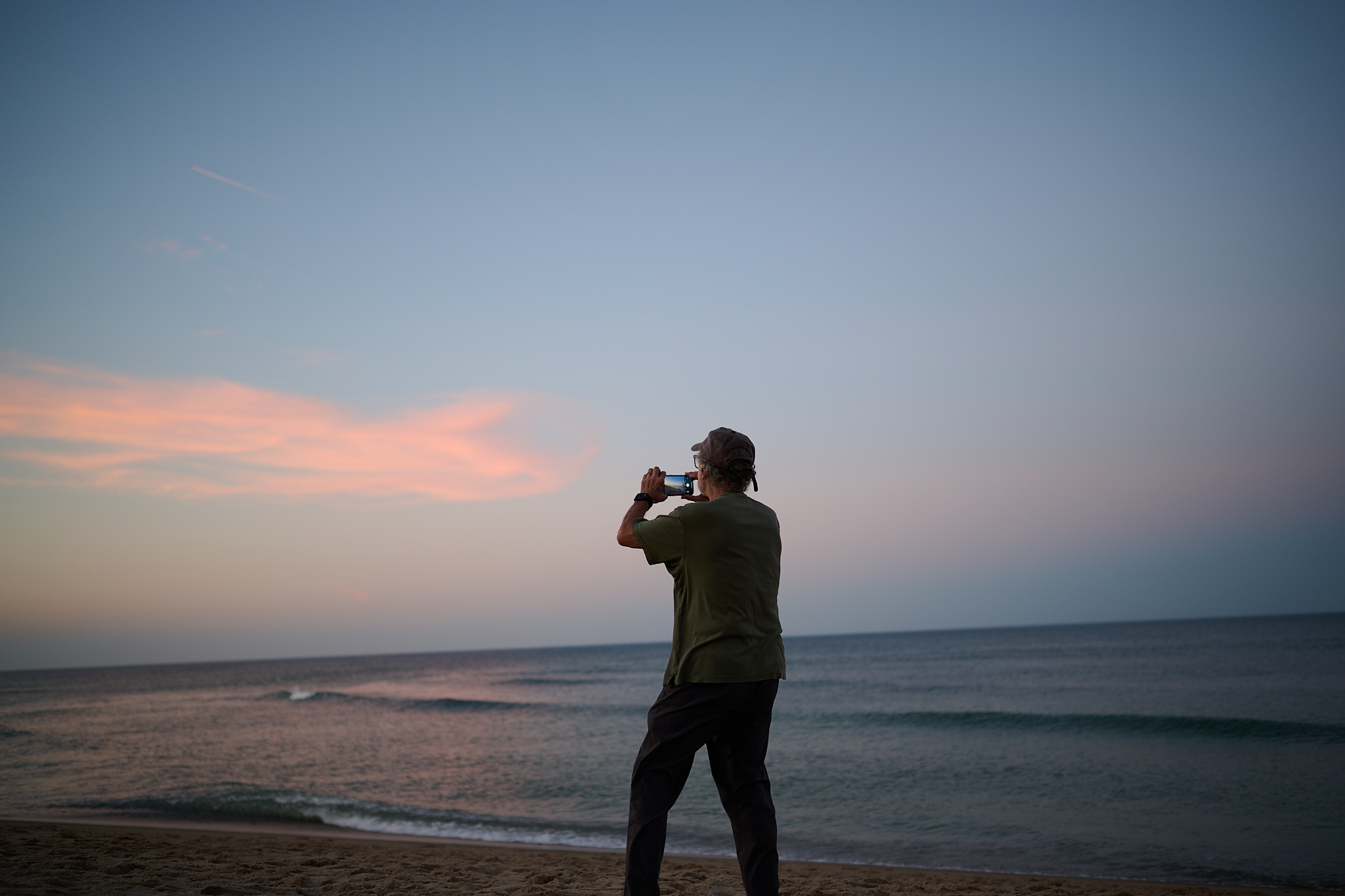 A man standing on a beach taking photos at sunset.