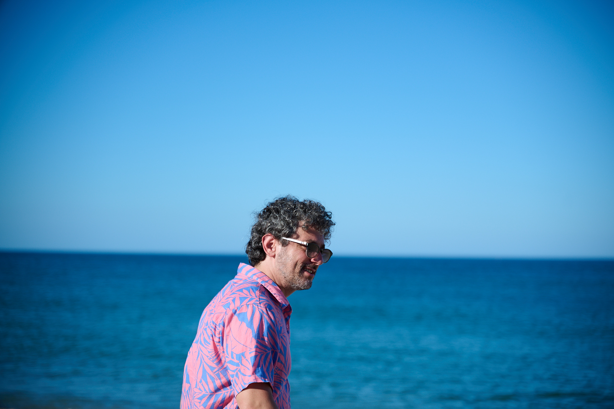 A man standing on the beach in the summertime with waves behind him.