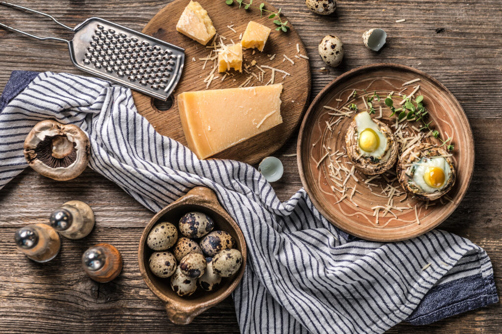 Stuffed mushrooms with quail eggs and parmesan cheese with food ingredients on aged wooden background, top view.